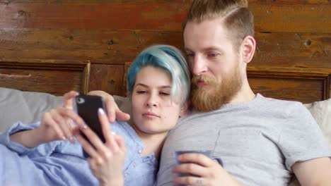 Pareja-hipster-con-teléfono-móvil-relajante-en-cama