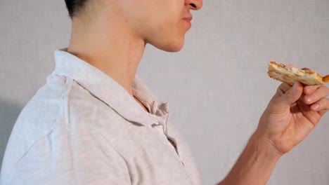 Young-man-eating-pizza-on-grey-background