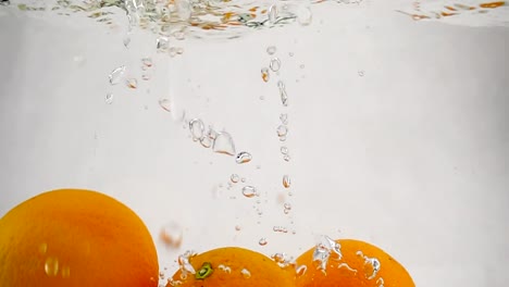 La-naranja-cayendo-en-el-agua-con-burbujas.-Video-en-cámara-lenta.-Frutas-en-aislaron-fondo-blanco.