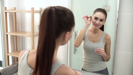 Belleza-maquillaje.-Cepillar-las-cejas-en-el-espejo-de-baño-de-mujer