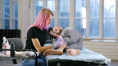 Artista-de-tatuaje-femenino-con-el-pelo-rosa-haciendo-tatuaje-en-el-estudio