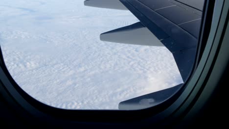 Wing-of-the-plane-through-the-porthole.-The-plane-flies-over-beautiful-air-clouds