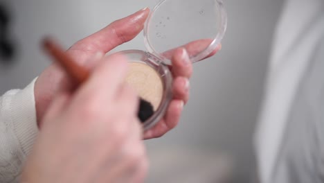 Woman-is-collecting-powder-on-a-brush-for-make-up,-close-up