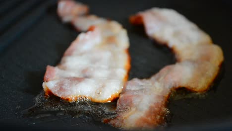 Close-up-of-a-slice-of-bacon-fried-on-a-hot-grill.