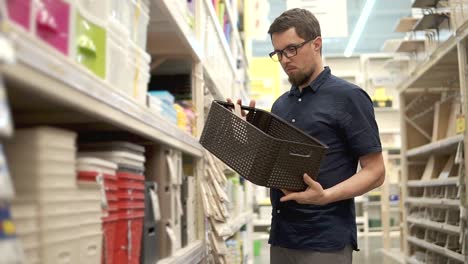 Man-is-watching-a-plastic-basket-in-a-supermarket,-twirling-it-in-hand