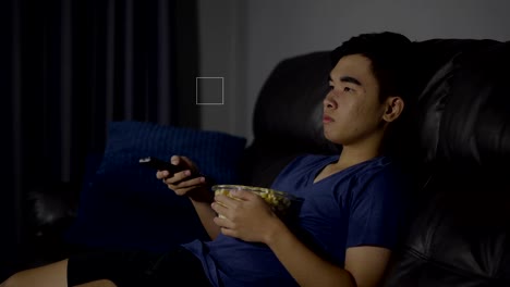 young-man-holding-remote-control-and-watching-TV-while-sitting-on-sofa-at-night