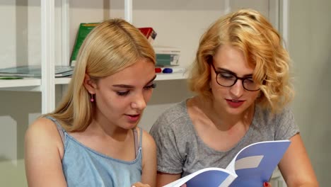 Young-female-students-reading-textbook-at-college-auditorium