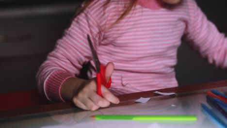 Close-up-shot-of-cute-little-girl's-hands-in-pink-sweater-cutting-paper-shapes-with-scissors-and-drawing-with-a-pencil