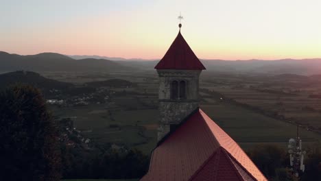 Vuelo-alrededor-de-la-iglesia-viejo-católica-sobre-una-colina-con-una-hermosa-vista-de-la-aldea-en-verano-en-la-puesta-del-sol