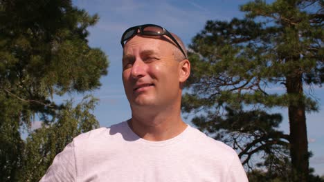 Bald-man-in-sunglasses-enjoying-coniferous-forest-on-trees-and-sky-background