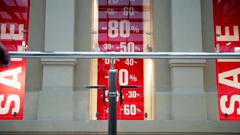 Lockdown-of-shopping-mall-with-discount-advertisement-in-window-displays-and-unrecognizable-female-customer-passing-by-camera-with-shopping-bags-in-her-hands