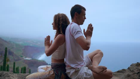 Mann-und-Frau-sitzen-auf-einem-Berg-auf-einem-Felsen-zurück-zu-meditieren-und-Yoga-auf-dem-Hintergrund-des-Ozeans-zu-tun.