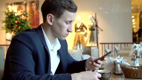 Young-handsome-man-with-phone-at-a-cafe-table