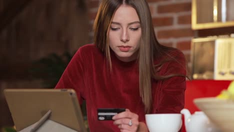 Young-woman-making-purchase-online,-typing-credit-card-details-on-tabletPC-in-the-modern-kitchen