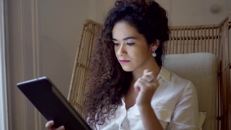 Thoughtful-girl-with-curly-hair-using-tablet-computer-at-home