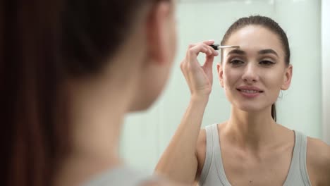 Schönheit-Make-up.-Frau-Bürsten-Augenbrauen-am-Badezimmerspiegel