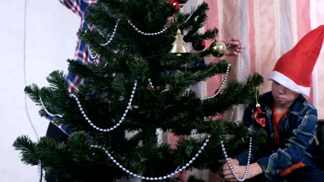 Mom-and-son-in-Christmas-hats-decorate-Christmas-tree-with-beads-and-balls.