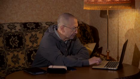 Grandpa-sitting-at-a-desk-and-working-at-a-laptop.-Is-typing.