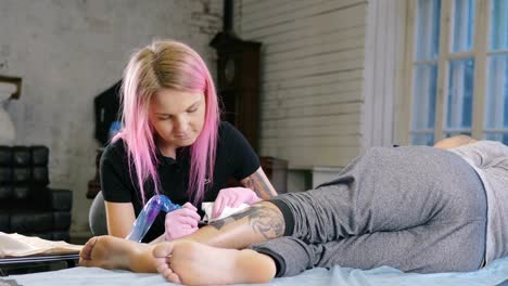 Female-tattoo-artist-with-pink-hair-making-tattoo-in-studio