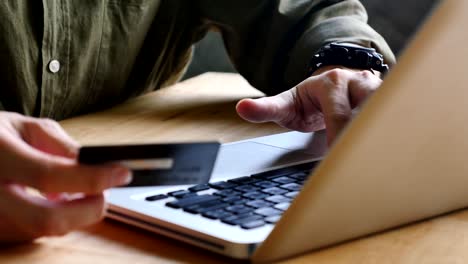 Close-up-of-male-hands-holding-a-credit-card-and-using-a-laptop-for-online-shopping.