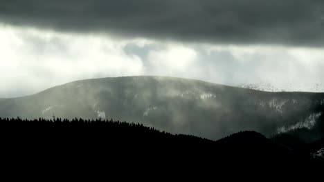 Time-lapse-thunder-clouds-moving-above-winter-mountain-range-dark-pine-forest-foreground-nature-landscape