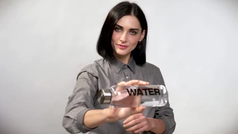 Young-pretty-woman-with-short-brown-hair-holding-and-pointing-bottle-with-water-in-camera,-showing-big-thumb,-happy,-white-background