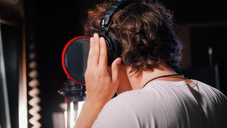 Young-handsome-singer-man-puts-on-headphones-in-the-studio.-Recording-new-melody-or-album.-Male-vocal-artist-with-curly-hair-preparing-for-working.-4k