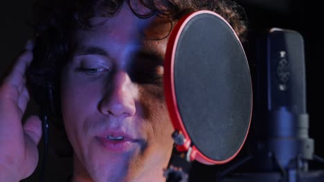 Young-handsome-singer-man-emotionally-writing-song-in-the-studio.-Recording-new-melody-or-album.-Male-vocal-artist-with-curly-hair-singing-alone.-Slow-motion.-4k