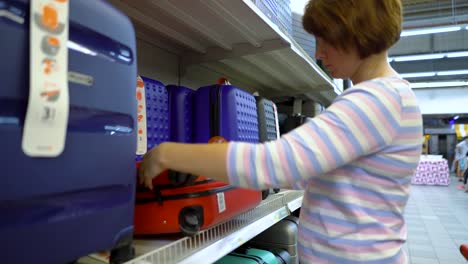 Caucasian-woman-near-shop-shelves-choosing-suitcase-in-haberdashery-market