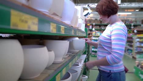 Caucasian-woman-near-shop-shelves-choosing-ceramic-pot-for-household-in-store