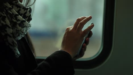 Primer-plano-de-mujer-sosteniendo-el-dispositivo-smartphone-mientras-viaja-en-tren.-Persona-navegando-por-internet-y-revisar-correos-electrónicos-en-el-transporte