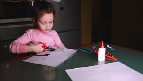 Beautiful-little-preschool-European-girl-in-pink-sweater-sitting-by-the-table-at-home-alone-cutting-shapes-from-paper