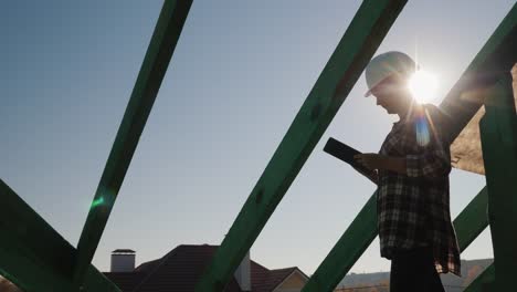 A-female-architect-is-working-with-a-tablet-on-the-roof-of-a-house.-Technical-and-author's-control-in-construction