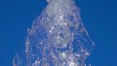 Un-chorrito-de-agua-y-hielo-claro.-Primer-plano-de-la-luz-que-salpica,-agua-de-fuente-soleado-en-el-parque-en-verano-sobre-fondo-de-cielo-azul.--Corriente-de-la-mosca-de-la-fuente-para-arriba-en-aire-con-muchas-salpicaduras.-Cámara-lenta.