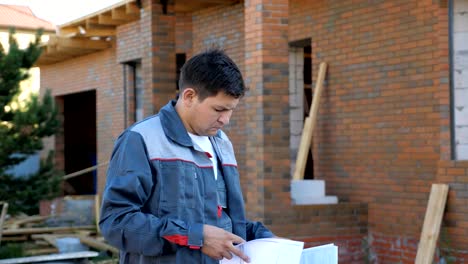 Adult-man-looking-at-paper-plans-standing-outdoors-of-building-under-construction,-slow-motion