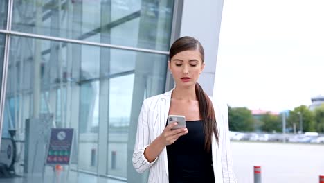 Hermosa-mujer-con-teléfono-caminando-cerca-de-oficina-de-negocios