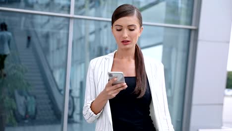 Hermosa-mujer-con-teléfono-caminando-cerca-de-oficina-de-negocios