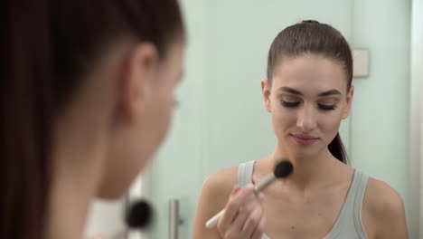 Maquillaje-de-la-cara.-Mujer-usando-polvo-y-mirando-en-el-espejo