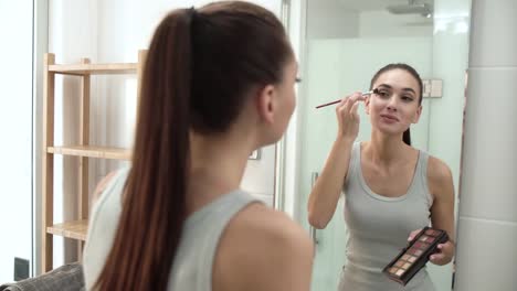 Maquillaje.-Mujer-aplicar-sombras-de-ojos-y-mirando-en-el-espejo