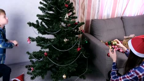 Mom-and-son-in-Christmas-hats-decorate-Christmas-tree-with-beads-and-balls.