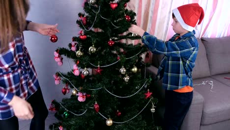 Mom-and-son-in-Christmas-hats-decorate-Christmas-tree-with-beads-and-balls.