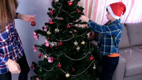 Mamá-e-hijo-en-sombreros-de-Navidad-decorar-árbol-de-Navidad-con-cuentas-y-bolas.