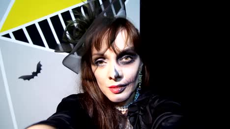 Halloween-party,-night,-frightening-portrait-of-a-woman-with-a-terrible-makeup-in-a-black-witch-suit,-croaks-in-front-of-the-camera