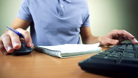 Cerca-de-las-manos-escribiendo-en-el-ratón-y-el-teclado-de-la-computadora.-Escribir-en-el-cuaderno