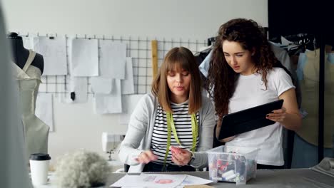 Joven-ropa-diseño-empresarios-observan-tablet-y-elegir-el-color-de-la-tela-para-la-ropa-en-el-bosquejo.-Sastre-está-tambaleándose-a-hilos-de-coser-y-aplicar-al-dibujo.