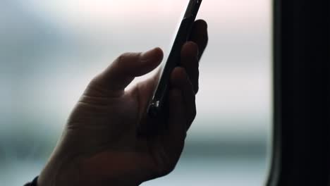 Rack-focus-on-cellphone-device-while-on-a-moving-train.-Close-up-of-hands-holding-smartphone-checking-emails-and-surfing-the-internet-while-on-commute