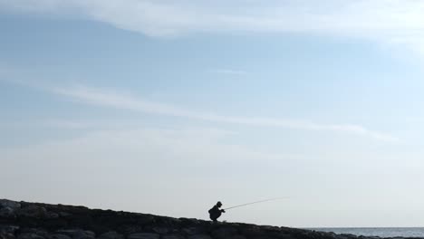 Pescador-sentado-en-dique-en-puesta-del-sol