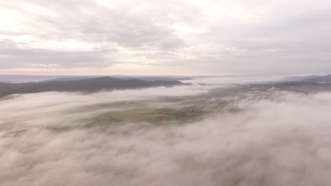 Low-clouds-and-fog-cover-Australian-farm-in-early-morning,-drone