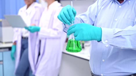 Scientists-working-in-lab-portrait.-Senior-chinese-male-scientist-working-in-lab,-stirring-a-flak-portrait-with-his-team-in-background.