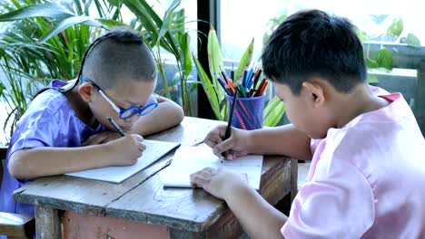 Happy-little-asian-boy-with-writing-in-notebook-and-pencils-drawing-at-home.-education-concept